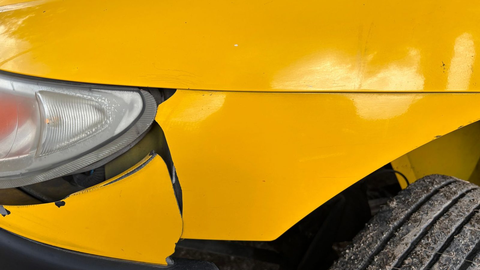Close-up of the damaged front bumper and headlight of a car after a collision.