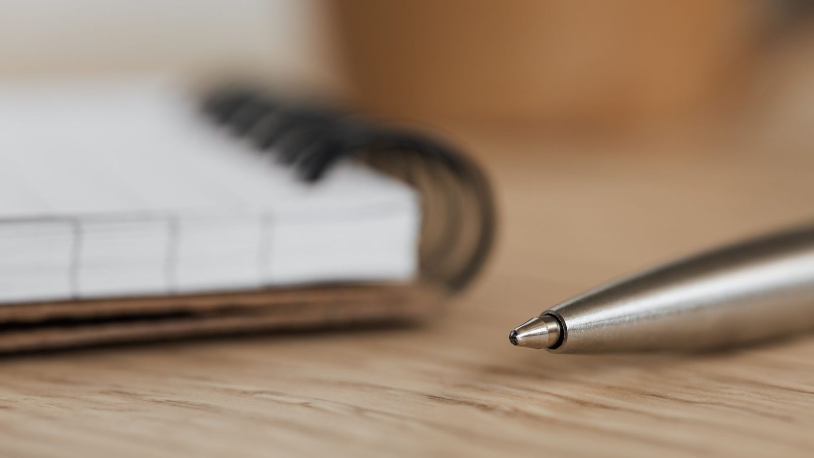 An open ring-bound notebook with blank pages and a ballpoint pen on a desk.