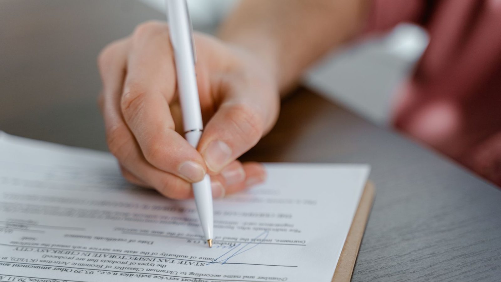 A hand signing an official document with a ballpoint pen.