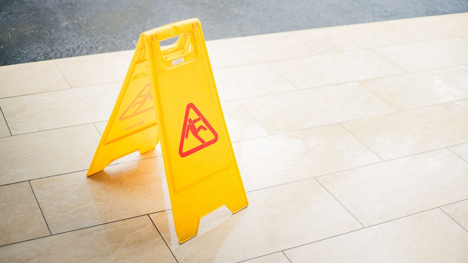 A yellow caution sign warning of a wet floor on tiled flooring.