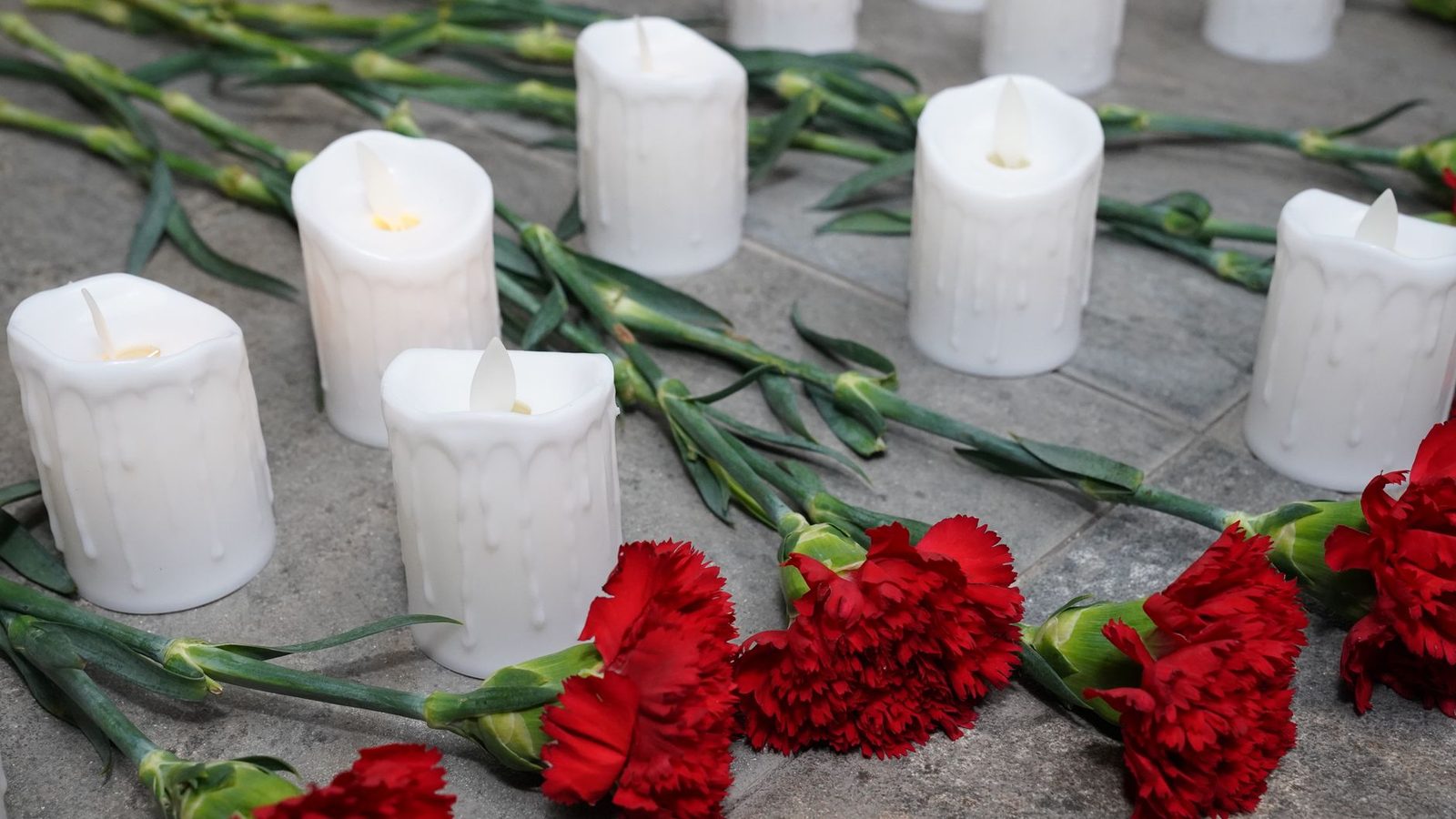 White candles and red carnations arranged on stone as a memorial.